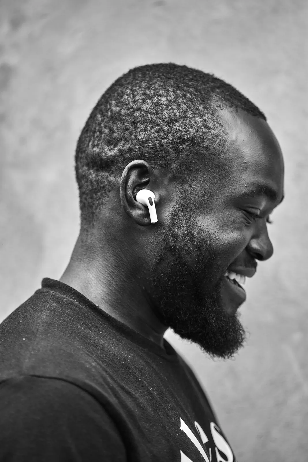 Black-and-white photo: a man seen in profile, smiling, wearing a wireless earbud.
